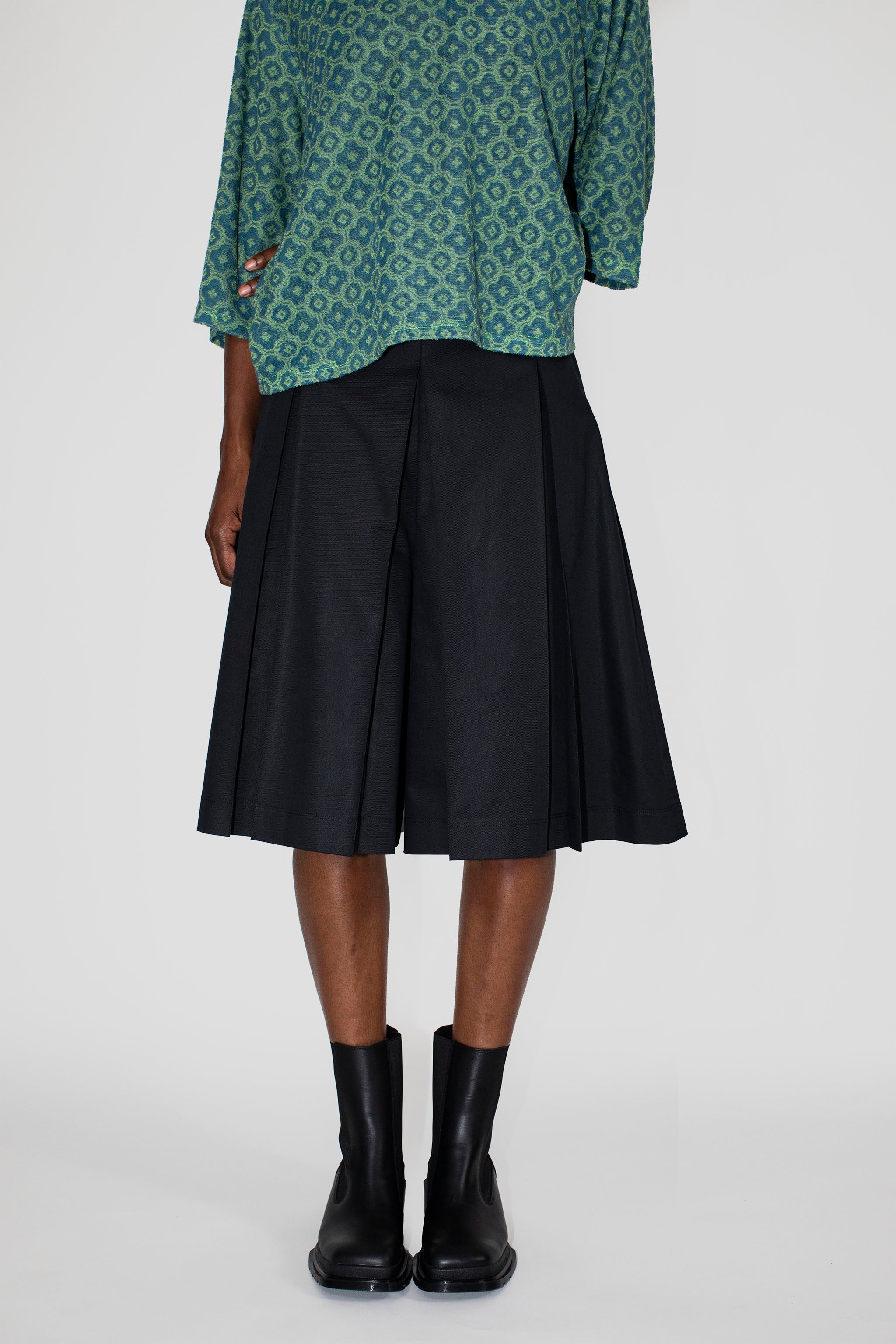 Person wearing a green patterned polo shirt and black skort on a white background