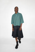 Person wearing a green patterned polo shirt and black skort on a white background