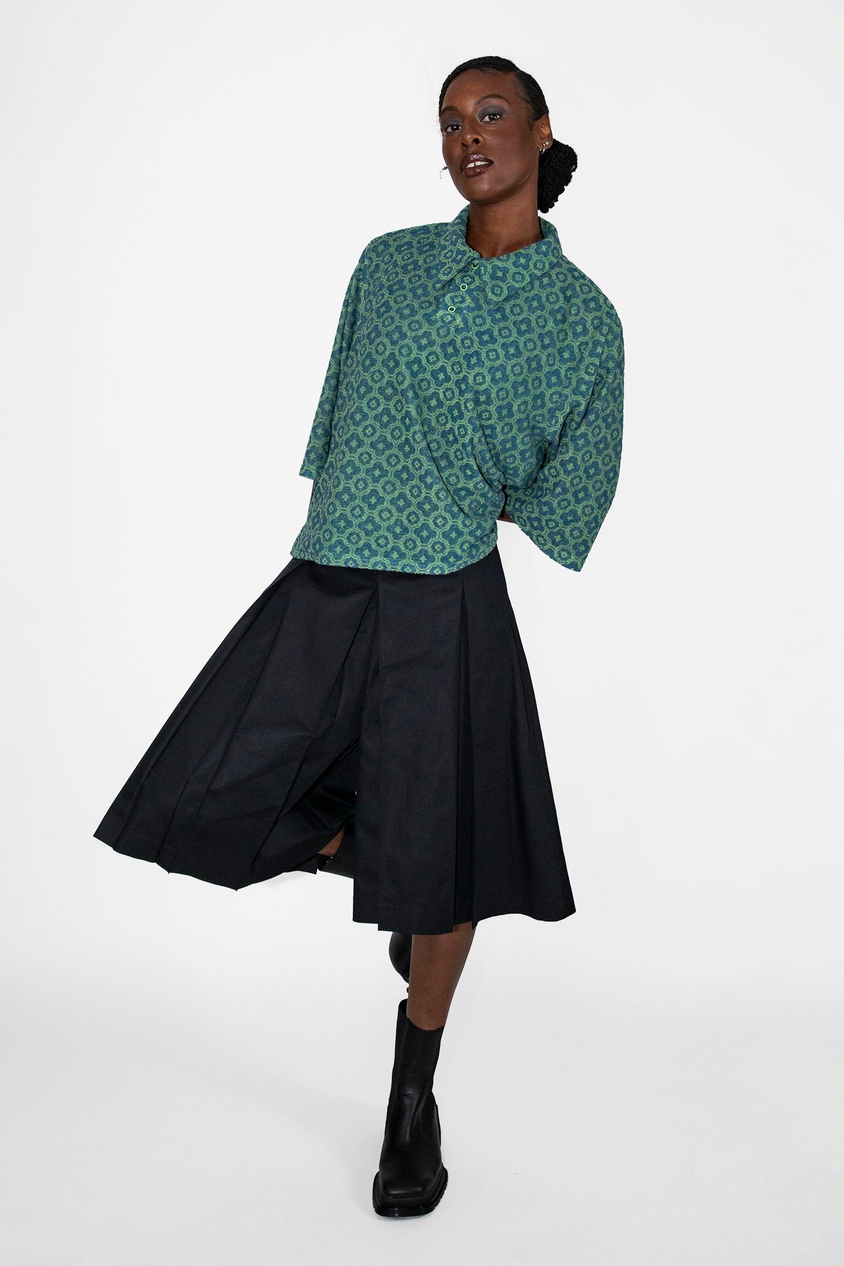 Woman wearing a green patterned polo shirt and black skort on a white background