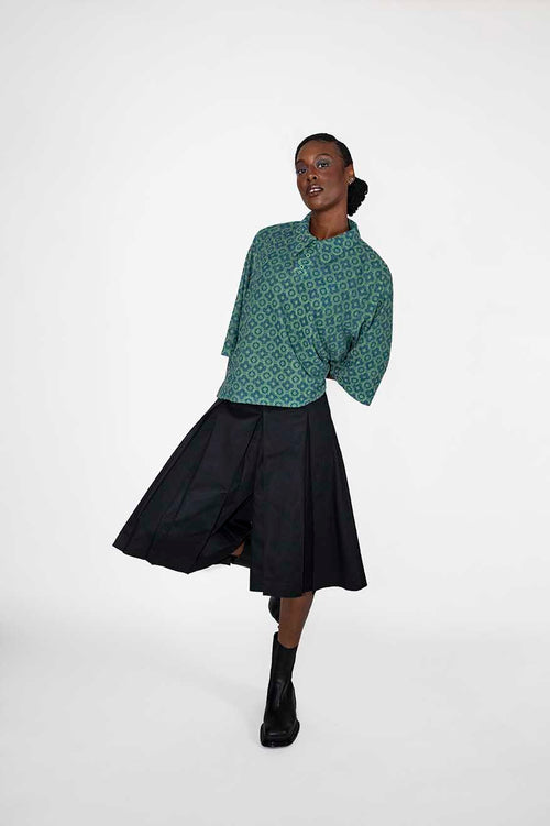 A model wearing a green patterned polo-tee and a black skort, standing against a plain white studio background.