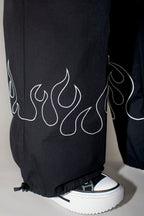 Black wide-leg pants with a white flame outline embroidery on the lower legs, worn with a black and white platform sneaker.