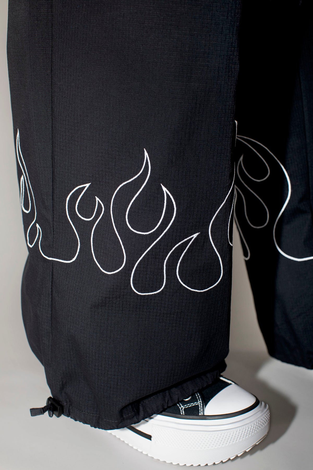 Black wide-leg pants with a white flame outline embroidery on the lower legs, worn with a black and white platform sneaker.