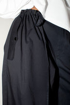 Close-up of a pair of loose black wide-leg trousers with a white shirt, showing the gathered drawstring waistband and side pocket.