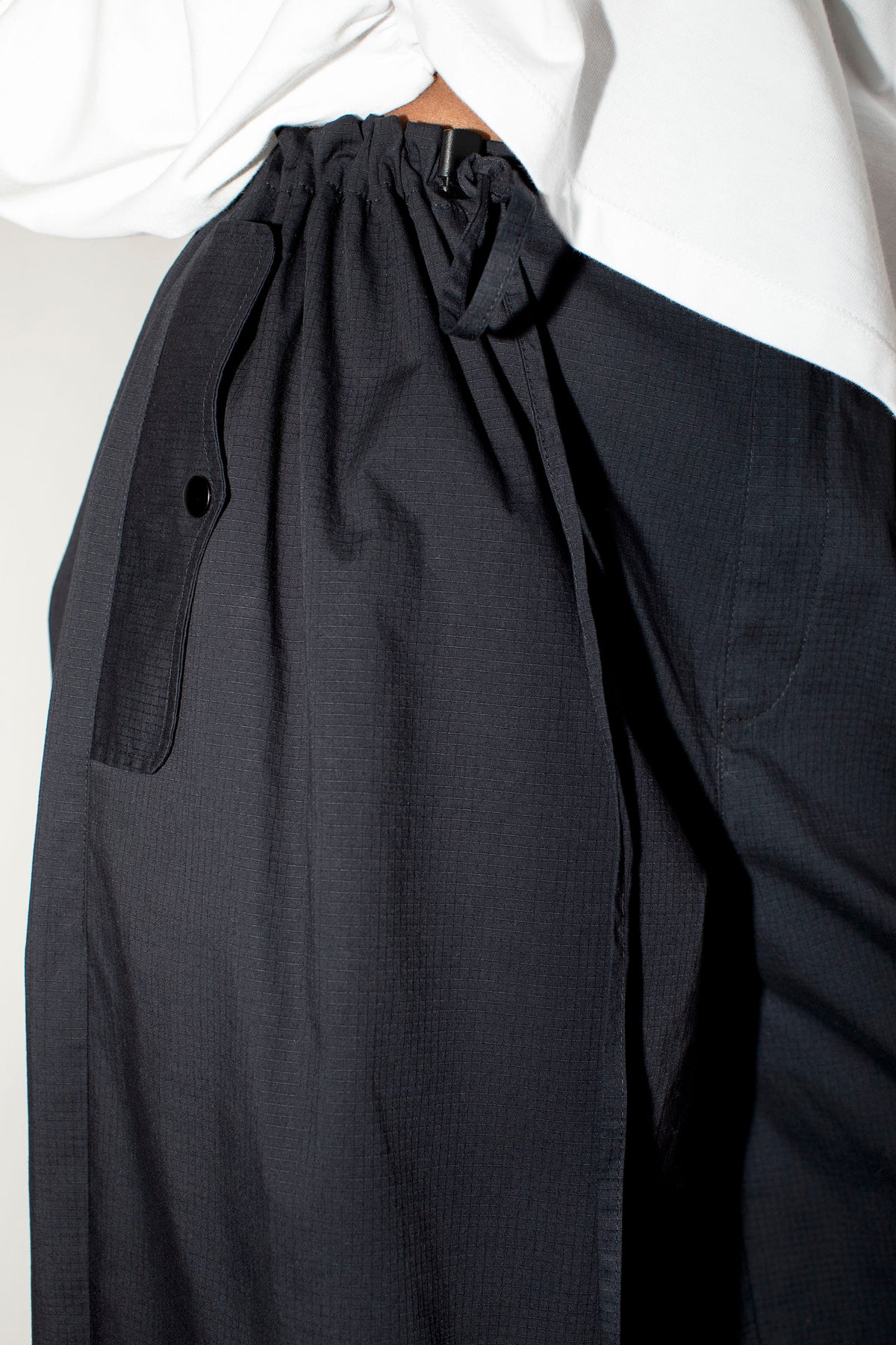 Close-up of a pair of loose black wide-leg trousers with a white shirt, showing the gathered drawstring waistband and side pocket.