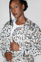 A model wearing a black and white abstract patterned trenchcoat over a white t-shirt, photographed against a plain light gray background.