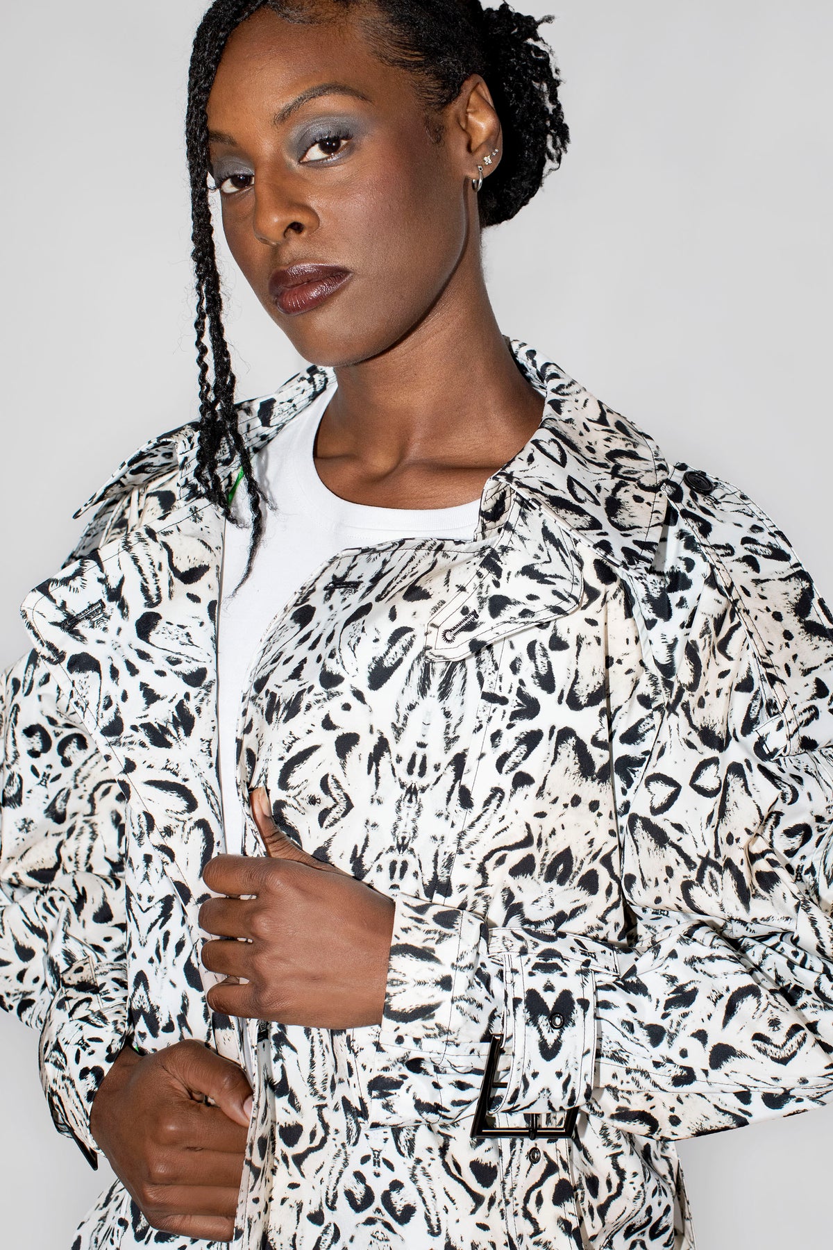 A model wearing a black and white abstract patterned trenchcoat over a white t-shirt, photographed against a plain light gray background.