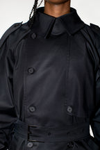 Close-up of a black double-breasted trench coat with a high collar and belt, worn by a model.