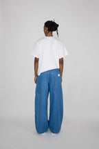 A person standing with their back to the camera, wearing a white short-sleeve t-shirt and wide-leg blue denim pants against a light gray studio background.
