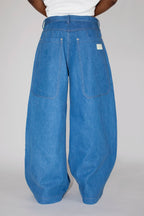 A person shown from the back wearing very wide-leg blue denim pants with a white top, photographed against a plain light gray studio background.