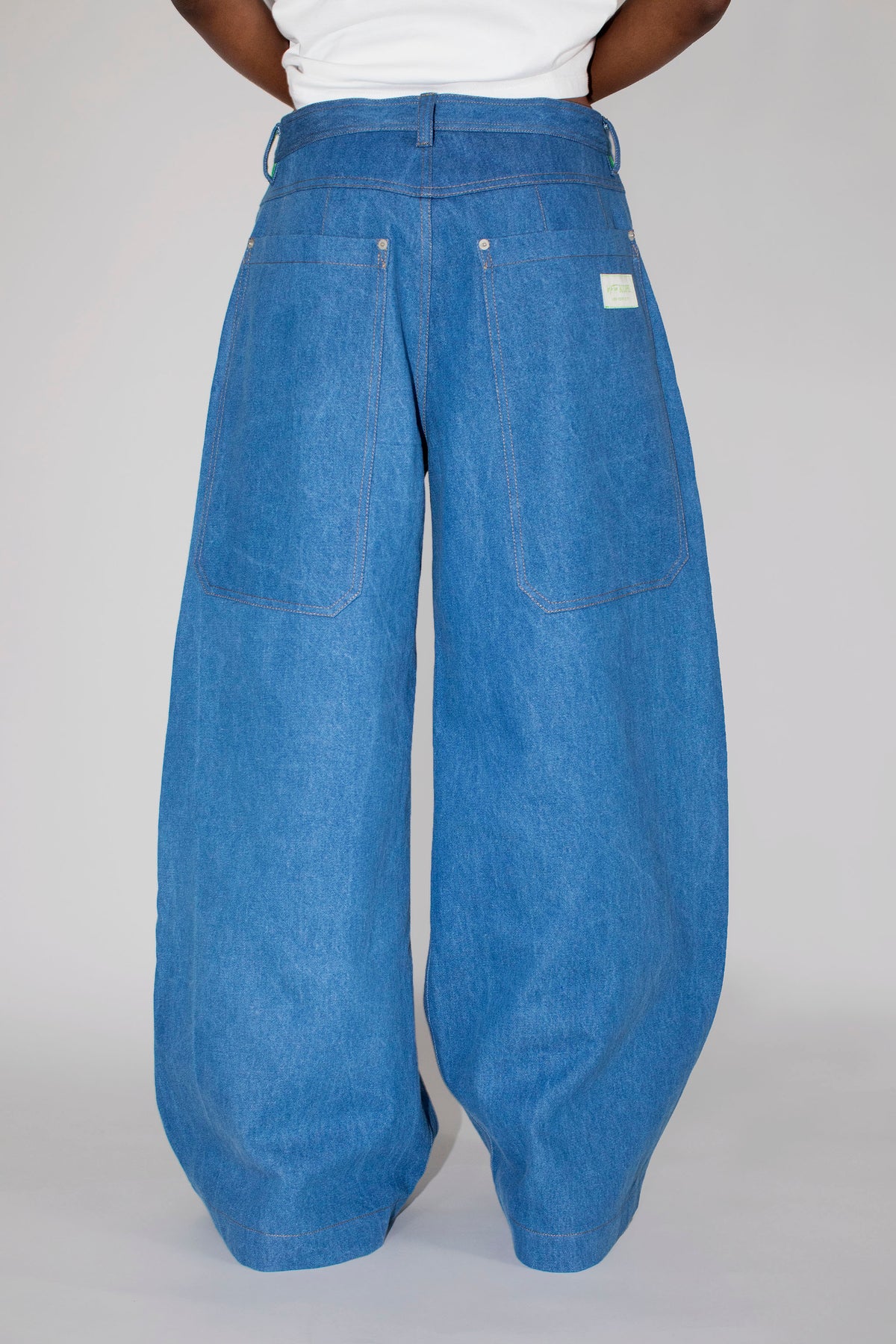 A person shown from the back wearing very wide-leg blue denim pants with a white top, photographed against a plain light gray studio background.