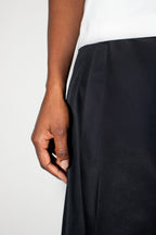 Close-up of a person wearing black wide-leg pants with a white top, showing the hand and waist area against a plain light background.