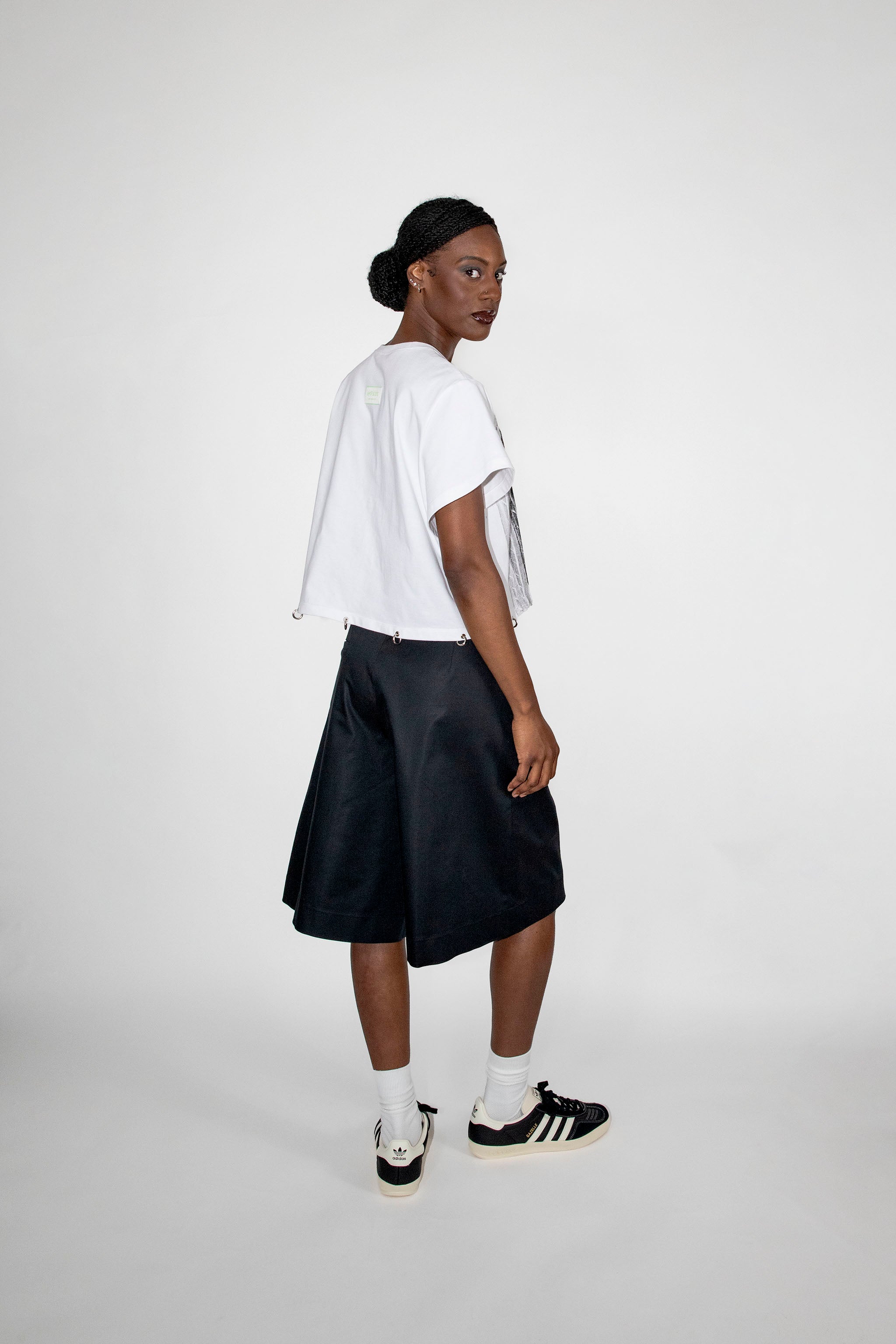 Person wearing a white t-shirt, black shorts, and black and white sneakers on a plain background
